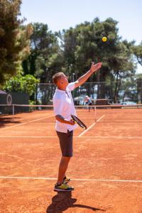 a man serving a tennis ball on a tennis court at Hotel Dražica - Hotel Resort Dražica in Krk