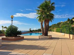 una piscina con due palme in un cortile di APPARTEMENT CLIMATISE - TERRASSE AVEC APERCU MER - GOLF DE ST TROPEZ a Les Issambres