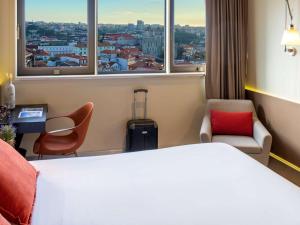 a hotel room with a bed and chairs and windows at Mercure Porto Centro Santa Catarina in Porto