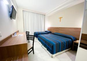 a bedroom with a bed and a table and a cross on the wall at Hotel Rainha do Brasil in Aparecida