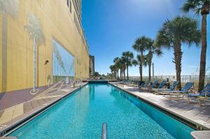 巴拿马城海滩Beachfront - Private Balcony - Near Pier - FLPCB62的建筑物旁边有带椅子和棕榈树的游泳池