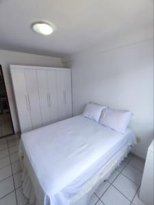 um quarto com uma cama grande com lençóis brancos e almofadas em Apartamento com piscina a uma quadra da praia de jatiuca em Maceió