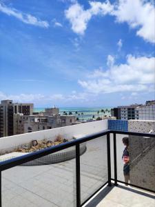 a young child standing on a balcony looking at the beach at Apartamento com piscina a uma quadra da praia de jatiuca in Maceió