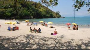 a group of people sitting on a beach with umbrellas at Apartamento Espaçoso Perto da Praia in Caraguatatuba