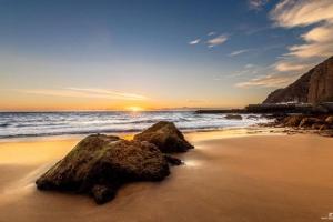 a beach with rocks on the sand and the ocean at PLAYA DEL NORTE VIVIENDA VACACIONAL in Gáldar