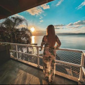 a woman standing on a balcony looking out at the ocean at Casa pé na areia para até 14 pessoas em bombinhas in Bombinhas