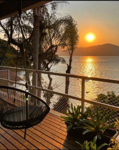a porch with a swing overlooking the ocean at sunset at Casa pé na areia para até 14 pessoas em bombinhas in Bombinhas