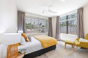 a bedroom with a bed and a chair and windows at 'Botanica Bonita' A Stylish Nightcliff Hideaway in Nightcliff