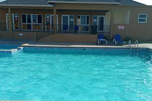 a swimming pool with blue chairs in front of a house at Home sweet home, Stonebrook Manor, Trelawny. in Falmouth