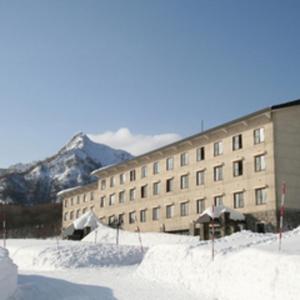 a large building with snow in front of a mountain at Kyukamura Oku-Daisen in Daisen
