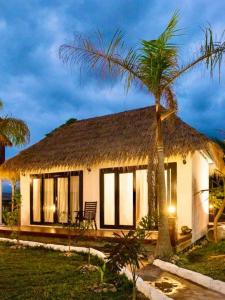 dom z dachem krytym strzechą i palmą w obiekcie Vang Vieng Savanh Sunset View Resort w mieście Vang Vieng