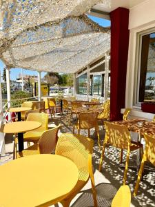 a restaurant with yellow tables and chairs and windows at Hôtel Clair de Lune in Mauguio