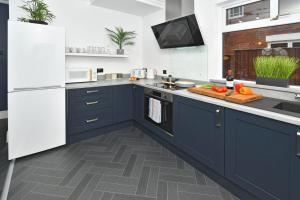 eine Küche mit blauen Schränken und einem weißen Kühlschrank in der Unterkunft Moonlight House - sleeps 7, driveway, garden in Crewe