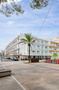 a large white building with a palm tree in a parking lot at Hostal Gami Adults Only in Cala Ratjada