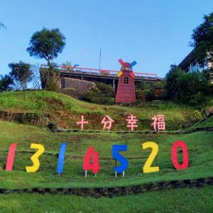 un cartello nell'erba con un mulino a vento sullo sfondo di Very Happy Homestay a Pingxi
