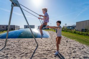 two young boys playing on a swing set on the beach at EuroParcs Enkhuizer Strand in Enkhuizen