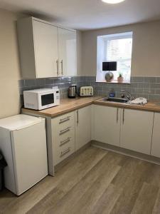 a kitchen with white cabinets and a microwave at Siop Iwan a Menna in Caernarfon