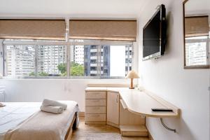 a bedroom with a desk and a bed and windows at Apê com janelão | 300 m da Av. Paulista in São Paulo