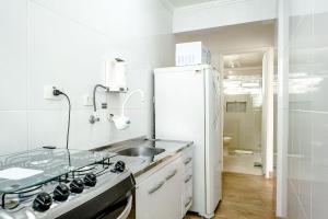 a white kitchen with a sink and a refrigerator at Apê com janelão | 300 m da Av. Paulista in São Paulo