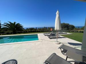 patio z parasolem i krzesłami oraz basenem w obiekcie Avithos Blue Villas w mieście Svoronata