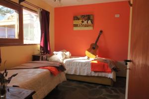 Un dormitorio con paredes de color naranja y una guitarra en una cama en Cabañas Yanasuy en Merlo