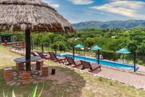 um resort com uma piscina com cadeiras e um guarda-sol de palha em Castelar - Hotel & Apart em Huerta Grande