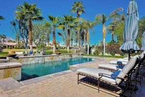 a pool with chairs and an umbrella and palm trees at Escape to Legends - Pool, Games & Amazing Mountain Views in PGA West #067651 5br in La Quinta