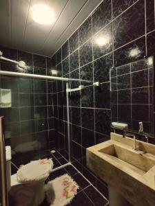 Baño de azulejos negros con lavabo y aseo en Casa com piscina no centro de Maragogi pertinho da praia!, en Maragogi