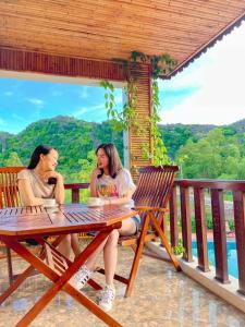 dos mujeres sentadas en una mesa hablando en sus celulares en Trang An Resort, en Ninh Binh