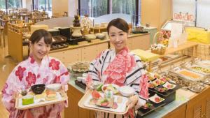 Kyukamura Nyuto-Onsenkyo في Senboku: امرأتين تحملان أطباق من الطعام في مطعم