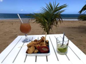 ein Teller mit Essen und ein Getränk auf einem Tisch am Strand in der Unterkunft Gîte Studio Marlin in Bouillante