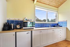 a kitchen with white cabinets and a window at Clovelly Cottage in Metung