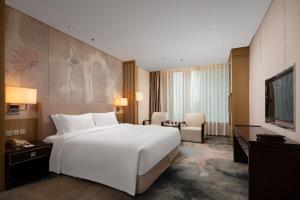 a bedroom with a large white bed and a television at The Yun Hotel Hankou in Wuhan