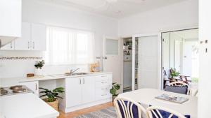 a kitchen with white cabinets and a table and chairs at Blue Beach House in Caloundra