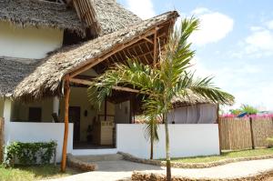 una casa con techo de paja y una palmera en Pole Pole Beach House, en Watamu