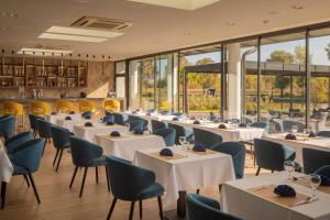 a restaurant with white tables and chairs and windows at Sziget Hotel in Nyíregyháza