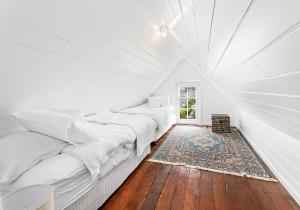 Habitación blanca con 3 camas y suelo de madera. en Boat Harbour Store Cottage, en Gerringong