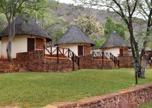 three huts with thatched roofs and a stone wall at Olifants River Lodge by Dream Resorts in Middelburg