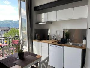 cocina con armarios blancos, mesa y balcón en Studio cosy, hyper centre d'Aix, vue montagnes, proche thermes, en Aix-les-Bains
