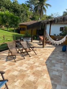 a patio with chairs and a hammock and a house at Picollo Bambino Suítes Ilhabela in Ilhabela