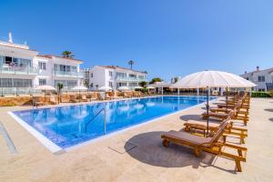 サルガールにあるNaranjos Resort Menorcaのラウンジチェアとパラソル付きのスイミングプールを併設しています。