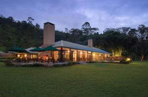 a building with tables and umbrellas in a field at Ceylon Tea Trails in Hatton