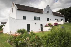 a white building with a black roof and some flowers at Zeekoegat Historical Homestead in Riversdale