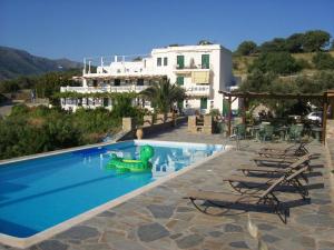a pool with chairs and a green inflatableigator in front of a building at Vassiliki Studios in Andros