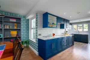 a blue kitchen with blue cabinets and a table at GuestReady - Moonbeam Cottage Quiet village in Eltham