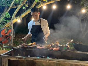 Ein Mann kocht Fleisch auf einem Grill in der Unterkunft Mường sang farmstay in Mộc Châu