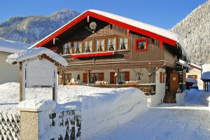 uma casa com um telhado vermelho na neve em Ferienwohnungen Merzer em Mittenwald