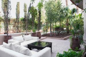 une terrasse avec des canapés blancs, une table et des arbres dans l'établissement Le Palais Rhoul and Spa, à Marrakech
