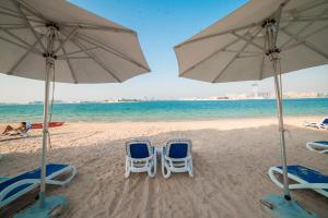 two beach chairs and umbrellas on a beach at 1-bedroom apartment with pool in Dubai