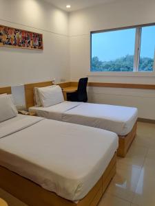 two beds in a room with a chair and a window at Mango Grove Hotel in Chandīgarh